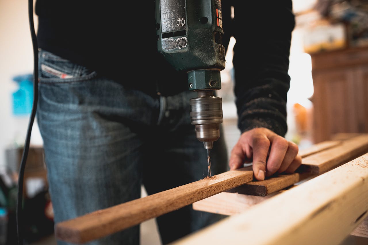 gallery-5 Close-up of a person using an electric drill on a wooden plank, showcasing detailed woodworking skills.