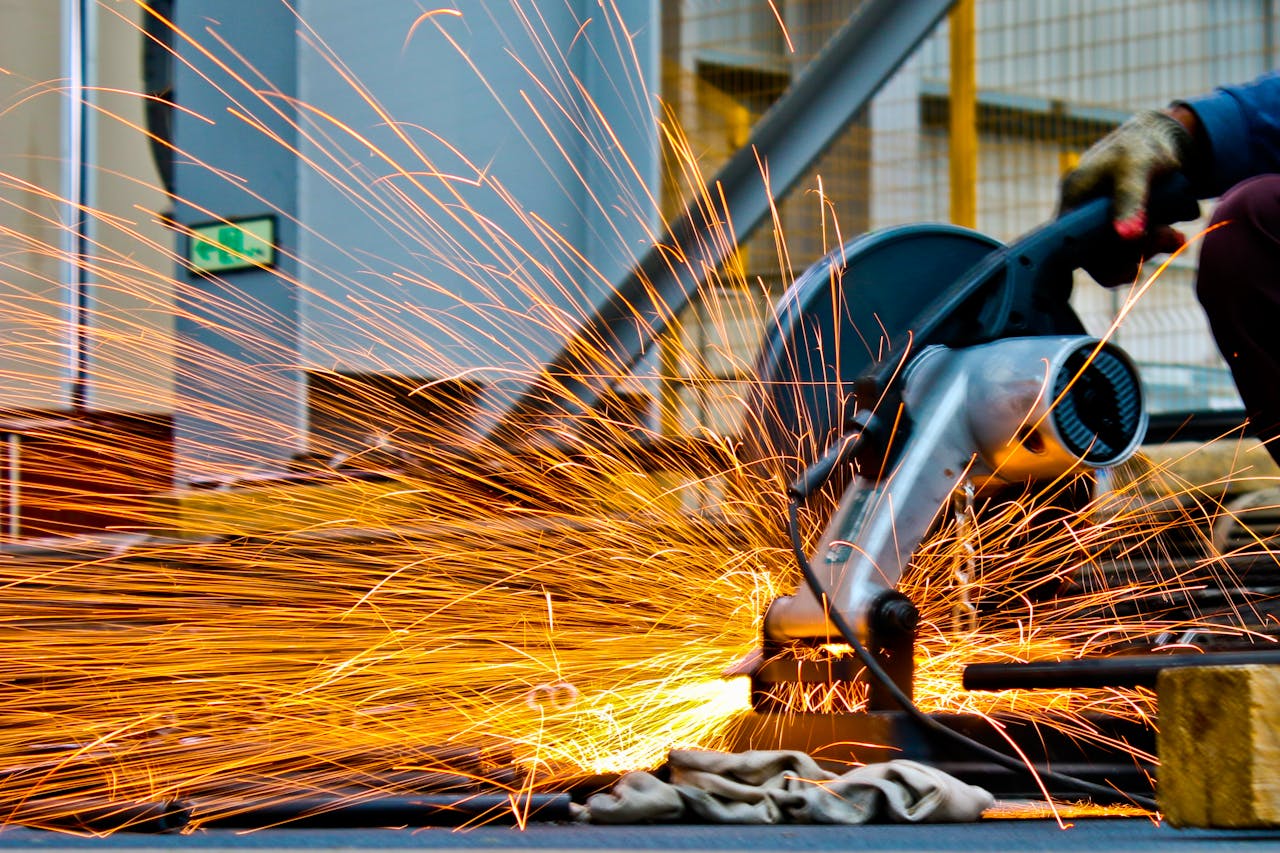 our-services-2 A worker operates a grinder cutting metal, creating a vibrant display of sparks in an industrial setting.