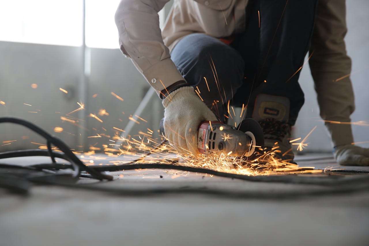 hero-img-01 A skilled industrial worker uses a grinder creating a burst of sparks indoors.