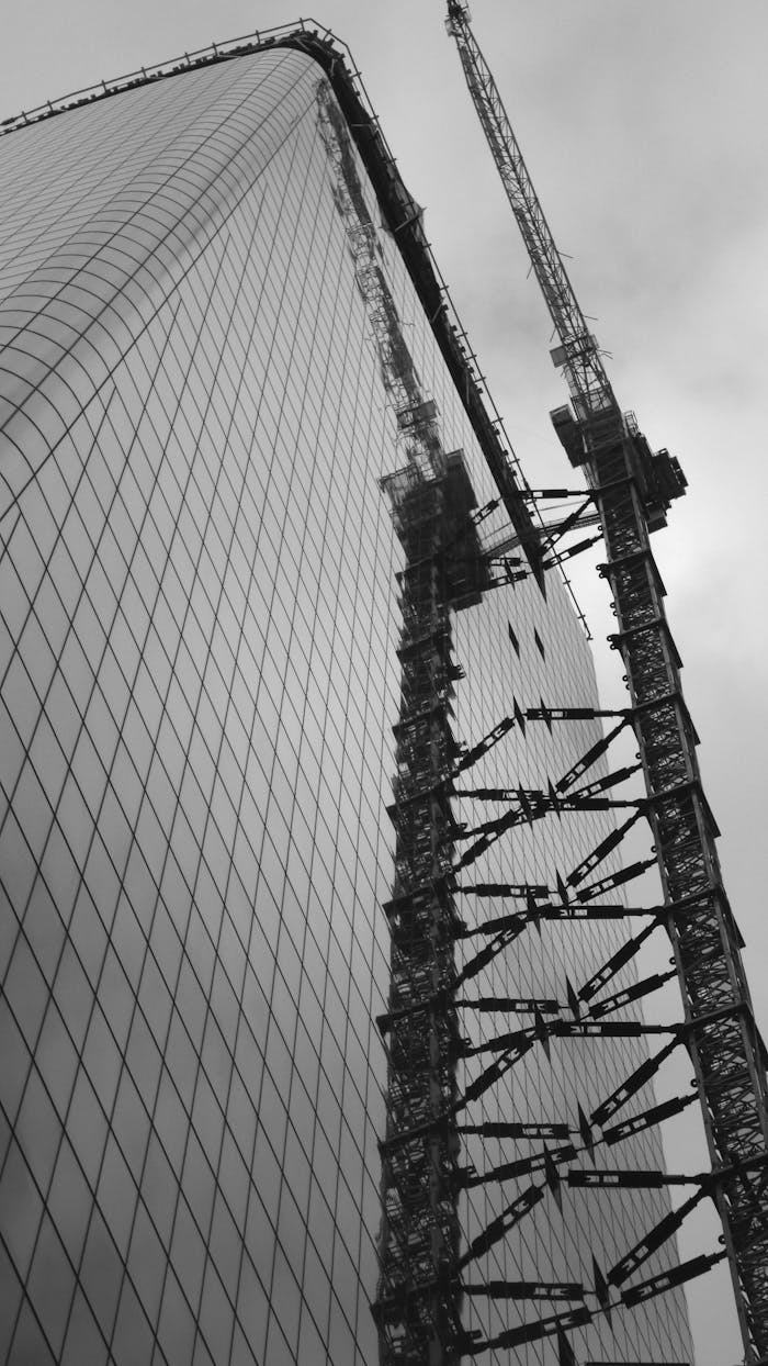 gallery-4 Low angle view of a skyscraper under construction with cranes, captured in monochrome.