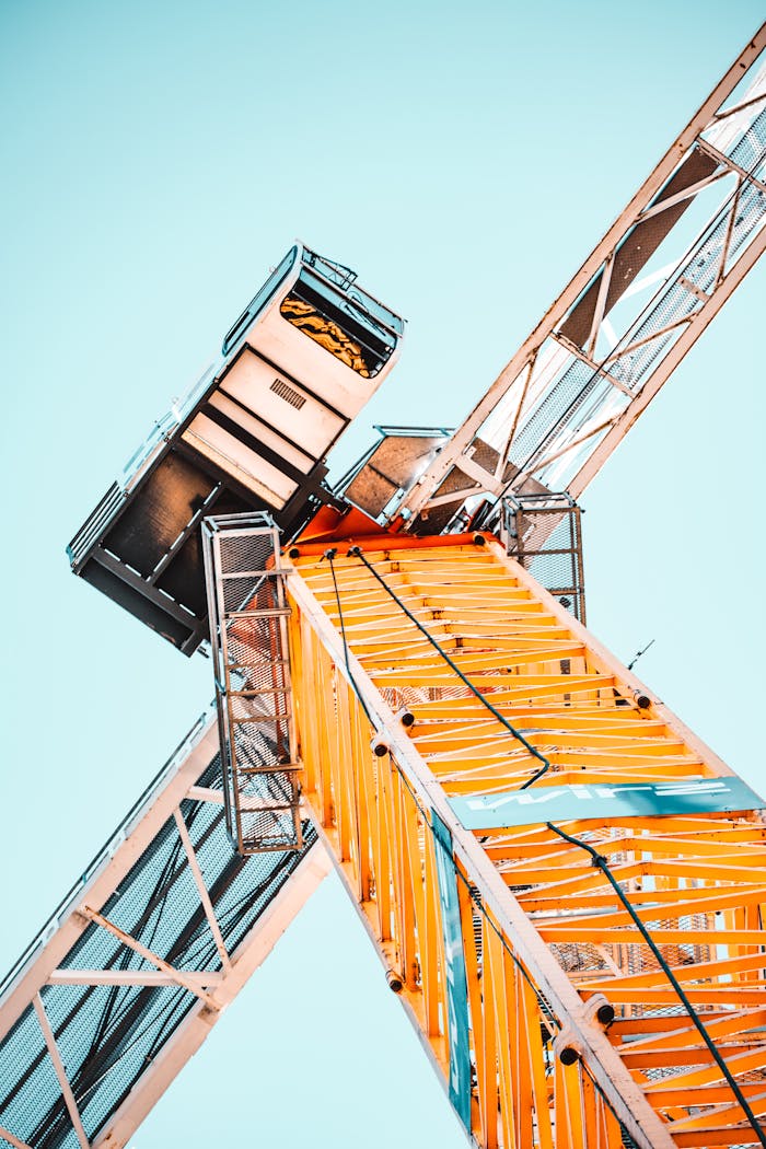 gallery-1 A striking low angle shot of a vibrant yellow tower crane against a clear sky, showcasing industrial power.