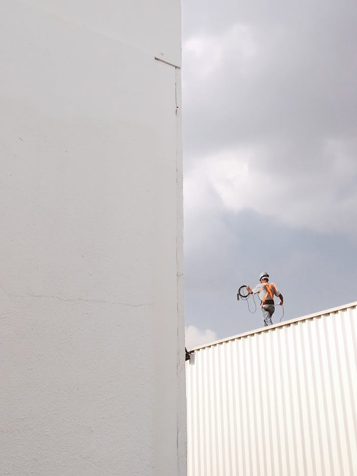 gallery-2 A construction worker stands on a rooftop against a large white wall, highlighting a minimalist aesthetic.